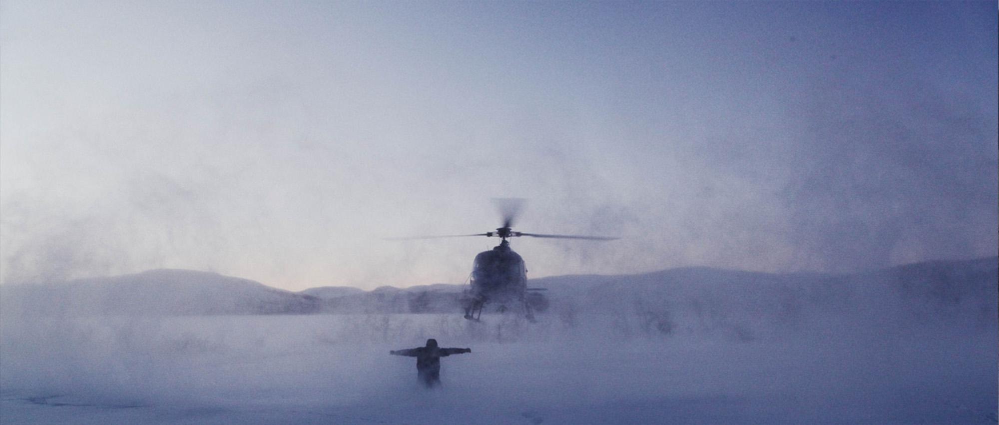 A landscape of snow and cliffs in the background with a helicopter and a person in front.