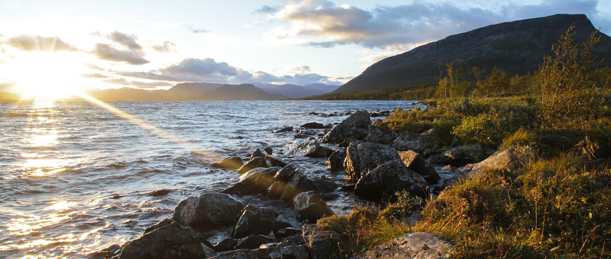 View of a sunset near water with mountains in the background in Lapland Finland.