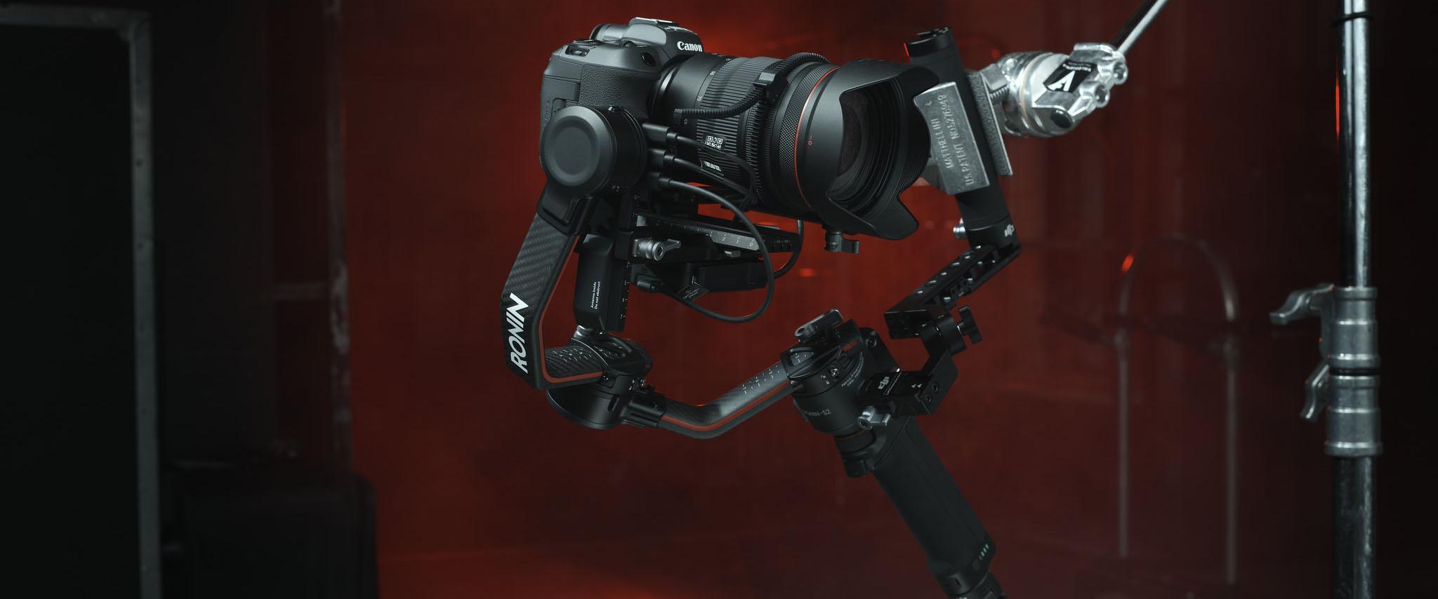 A professional filming setup with a Canon camera and a Ronin Rs2 in front of a red background.