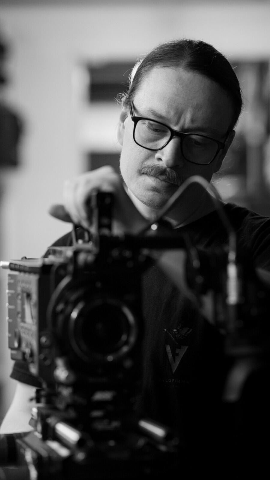 Man in glasses standing behind a camera